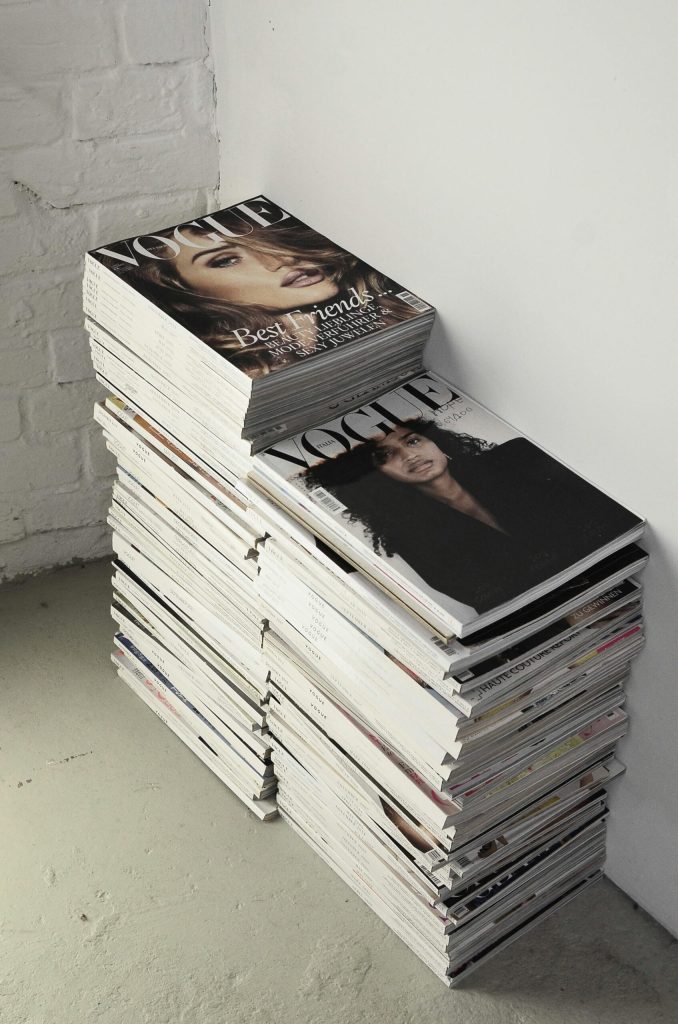 High angle many fashion magazines stacked on floor against white brick wall in studio